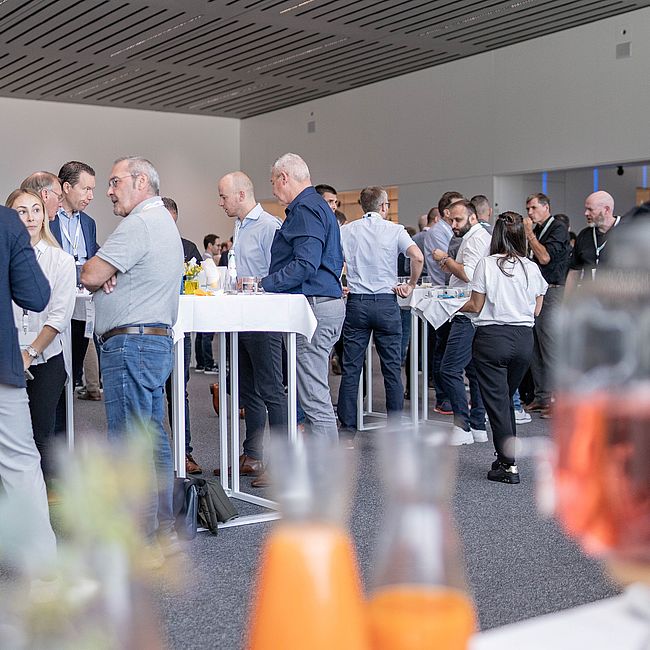 Geschäftsleute im Gespräch an Stehtischen bei einem Networking-Event in einem modernen Veranstaltungsraum
